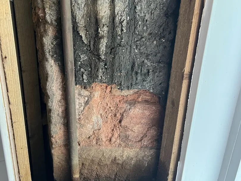 Wall void beside the bathroom window with a pipe and damp-blackened stonework