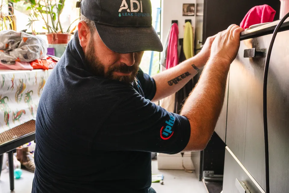 ADI engineer tracing pipework behind a kitchen cabinet